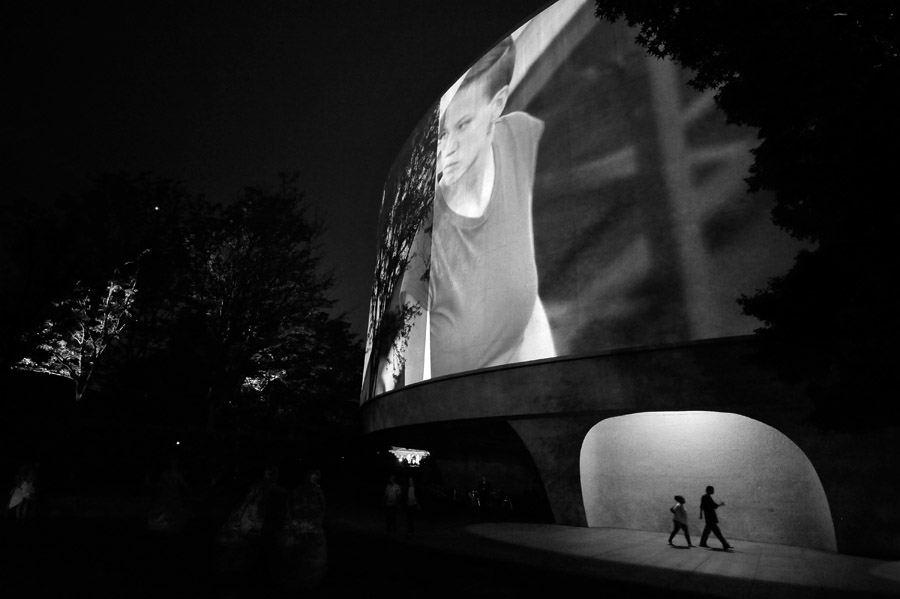 People walk around the outside of the Smithsonian Hirshhorn Museum as Doug Aitken's {quote}Song 1{quote} is projected on the outside of the building on Sunday May 13, 2012 in Washington, DC.  