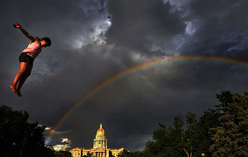 A rainbow extends over the state capitol as Destiny Caceres, 10, of Albuquerque, New Mexico leaps from the Stunt Jump attraction Saturday 06/05/10 during People's Fair at Civic Center Park in downtown Denver, Colo. Photo by Matt McClain  