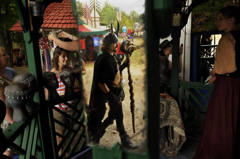 Philip Doccolo, center, is reflected in a mirror as he walks by the Valkyrie's Armourer as Kellie Stone, left center, is fitted for goods as Sally Mayer, right, looks on during the annual Maryland Renaissance Festival on Sunday September 02, 2012 in Crownsville, MD.  The festival is open on Labor Day and then Saturdays and Sundays from 10 a.m.-7 p.m.  It runs through October 21st.  (Photo by Matt McClain for The Washington Post)