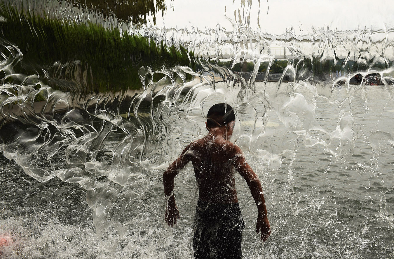 A boy cools off from the heat under a waterfall feature at the Yards Park on Thursday August 21, 2014 in Washington, DC.  (Photo by Matt McClain/ The Washington Post)