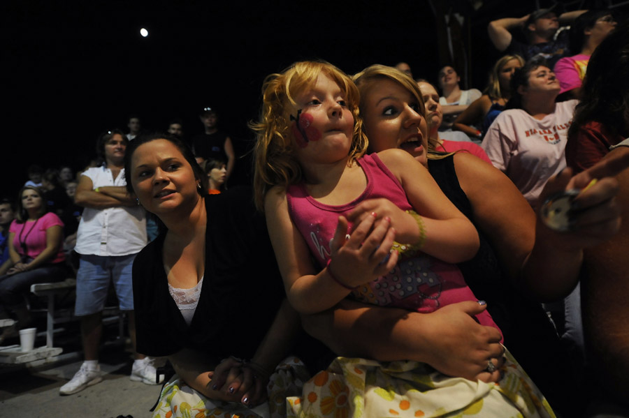 Kayla Kelley, left, sits next to Savannah Himelright, 6, center, as she is held by her aunt, Brittney Herald, right, as they watch cars collide during the demolition derby at the Shenandoah County Fair on Monday August 27, 2012 in Woodstock, VA.  