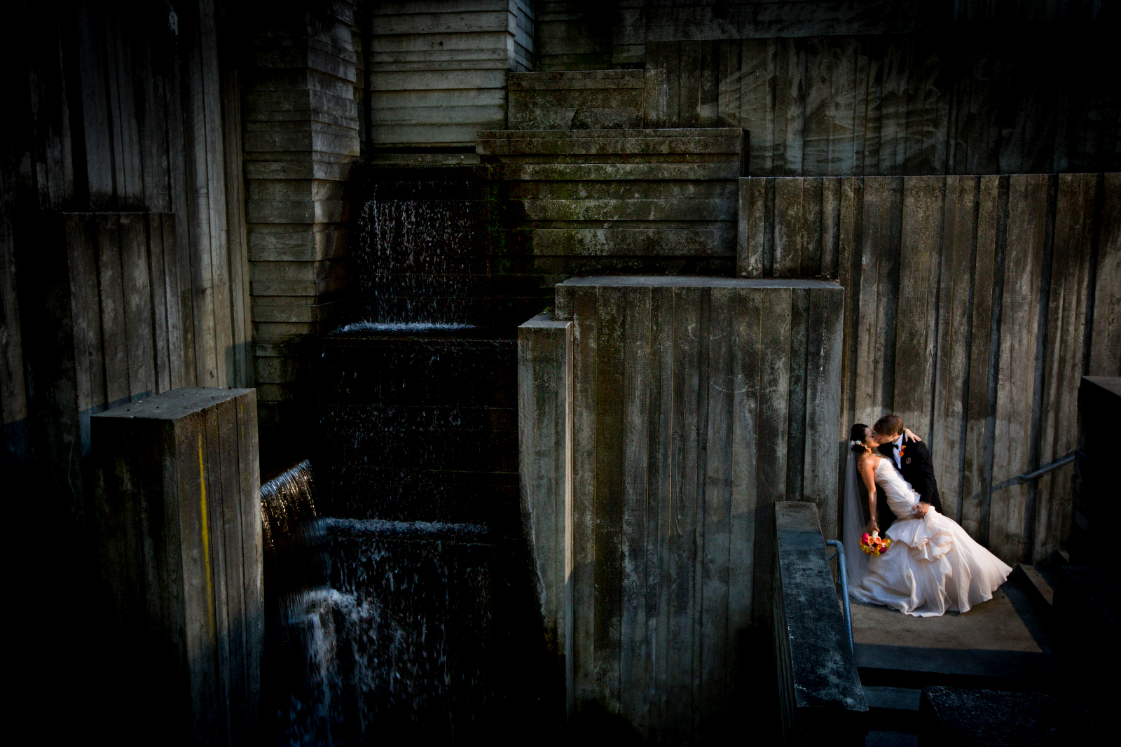 The bride & groom kiss at the waterfall at Freeway Park in Seattle prior to their wedding at the Seattle Aquarium. (Wedding Photography by Scott Eklund/Red Box Pictures)