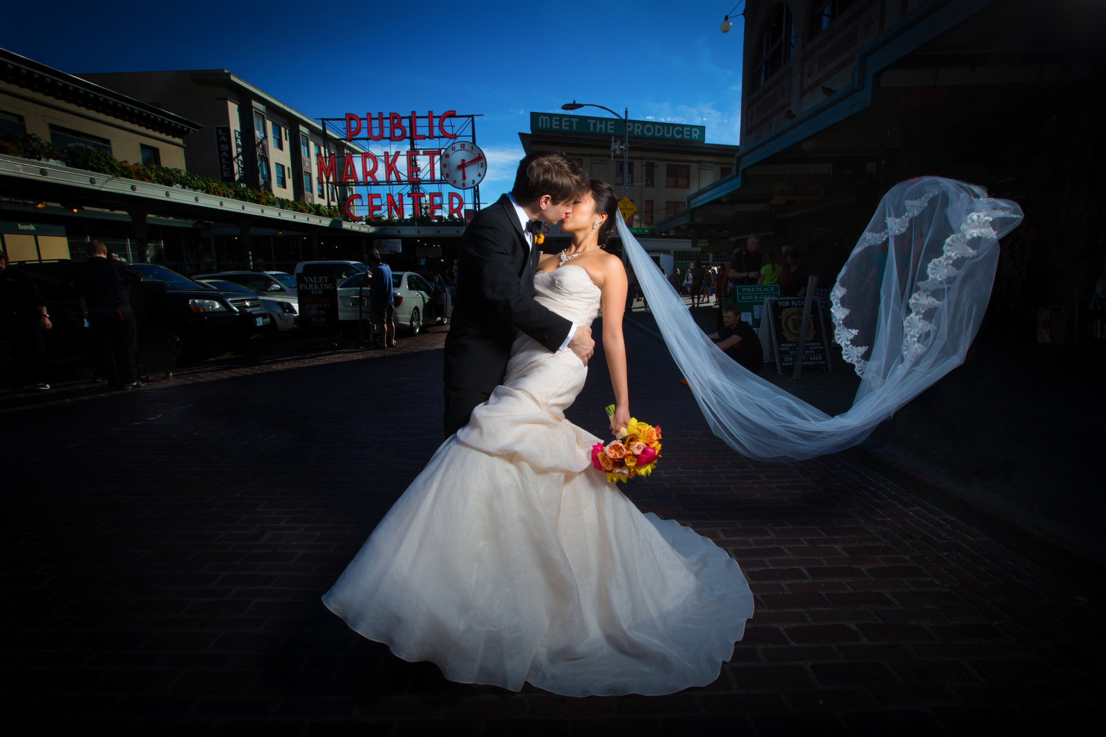 A gust of wind catches the veil as the bride & groom kiss at the Pike Place Market prior to their wedding at the Seattle Aquarium. (Wedding Photography by Scott Eklund/Red Box Pictures)