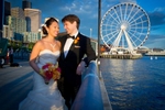 A portrait of the bride & groom in front of the Great Seattle Wheel on the waterfront during their wedding at the Seattle Aquarium. (Wedding Photography by Scott Eklund - Red Box Pictures)