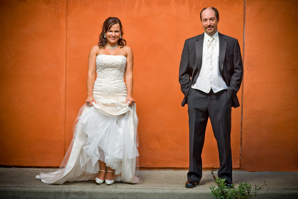 Michelle & Matt have their portrait taken in front of an orange stucco wall near their wedding venue at The Attic in Sumner, WA. (Photography by Scott Eklund/Red Box Pictures)