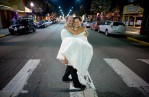 The wedding couple was all smiles as Matt carries his bride Michelle, in her bare feet, across the crosswalk on Main Street in Sumner, WA after their wedding and reception at The Attic. (Photography by Scott Eklund/Red Box Pictures)