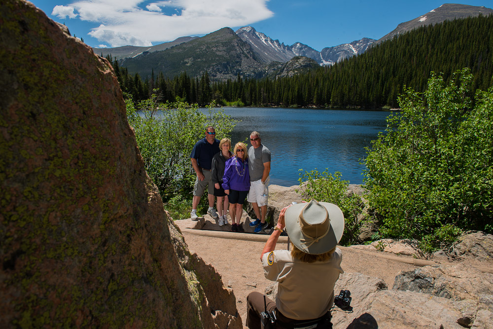 Volunteer Terri Morrow takes a picture for a family visting Bear Lake in Rocky Mountain National Park. The photo spot is the location from which the image on the back of the Colorado quarter is taken.