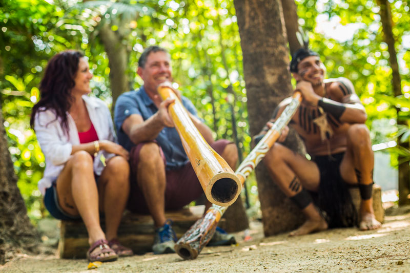 A tourist couple getting a didgeridoo lesson by indigenous performer at Tjapukai Aboriginal Cultural Park, Cairns