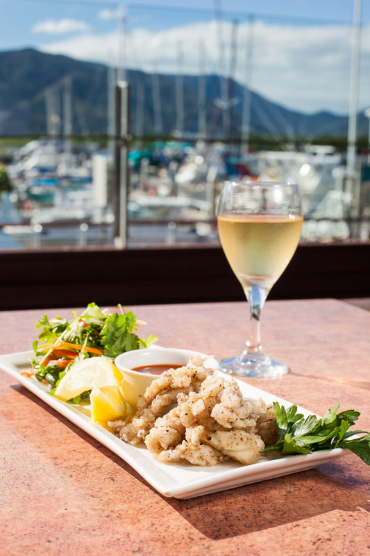 Dish of salt and pepper squid with glass of wine overlooking the marina in Cairns