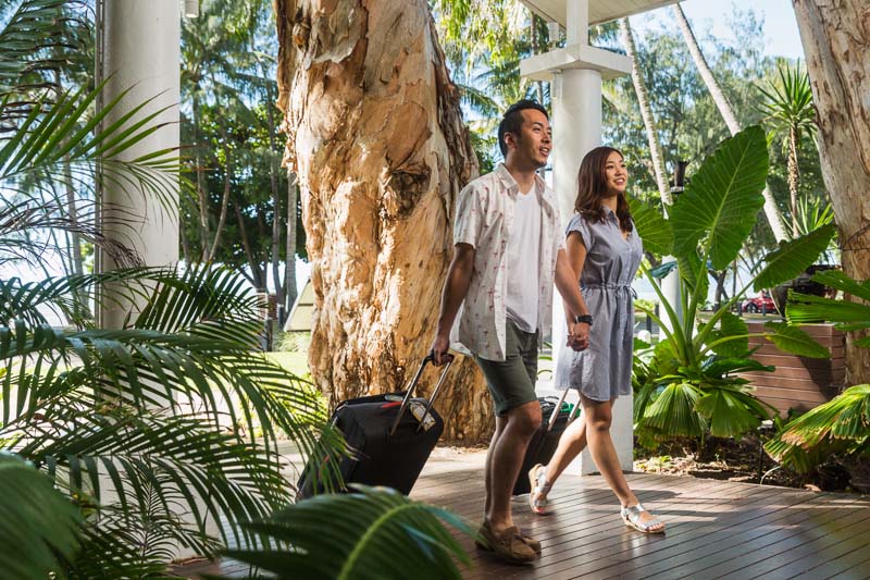 Asian couple walking with luggage at The Reef House, Palm Cove