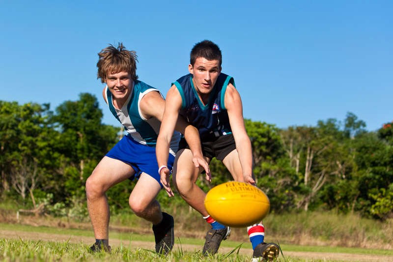 Two male students jostling for the AFL ball on the sports field, Cairns