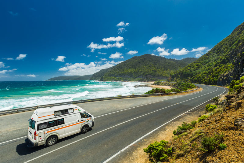 A campervan driving along a beautiful coastal road with blue skies