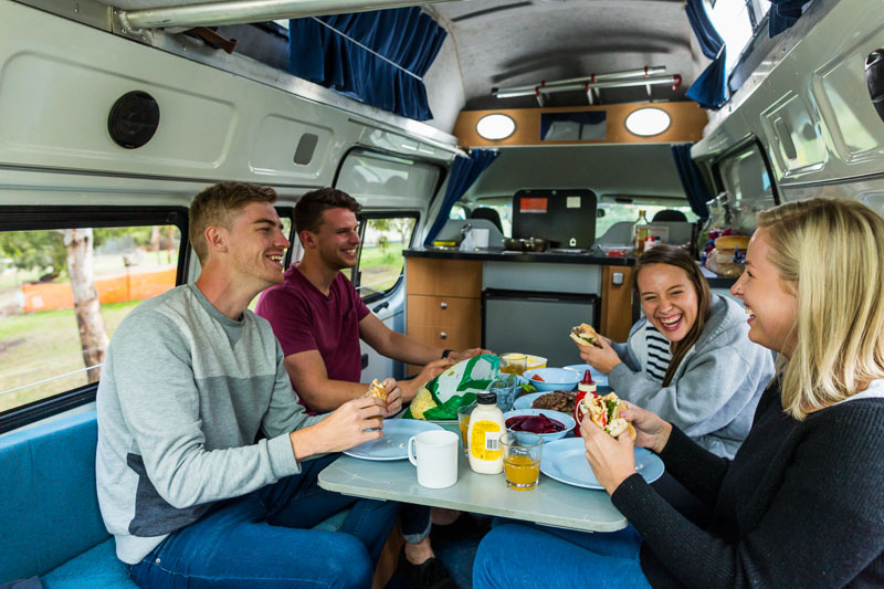 A group of young travellers eating dinner inside a campervan