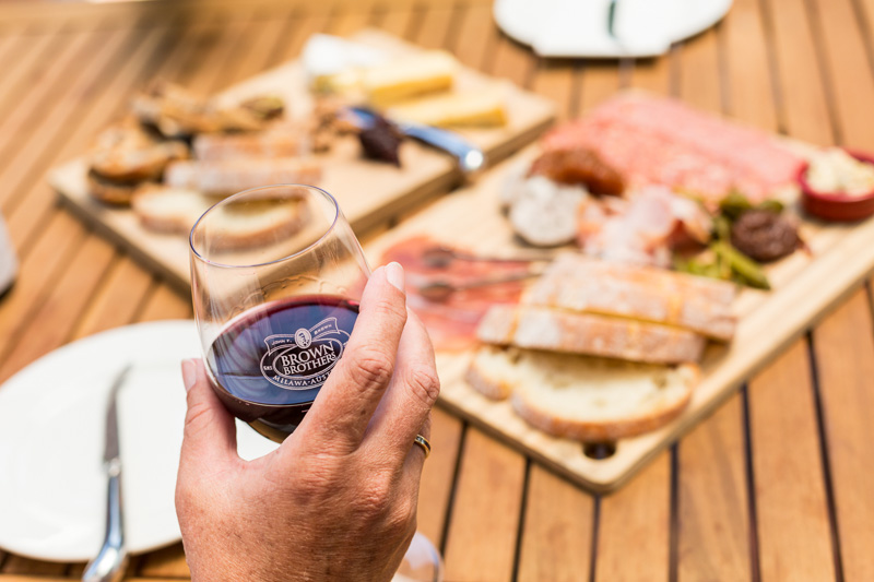 Hand holding wine glass with food platter in backgroudn at Brown Brothers in Milawa, Victoria