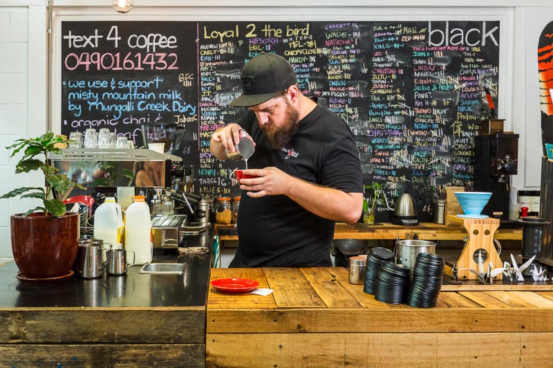 A cafe barista at counter pouring crema into an espresso coffee