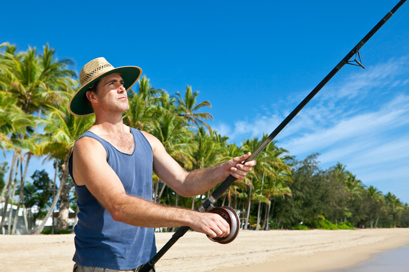 Man holding a fishing rod on a tropical beach
