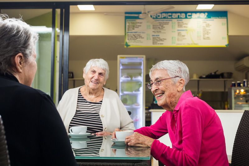 Elderly women smiling and chatting over coffee at a retirement village cafe
