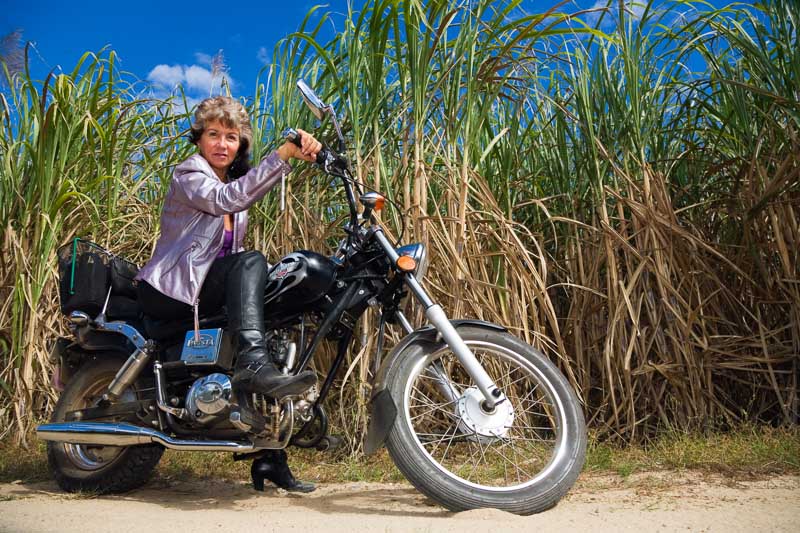 Portrait of woman seated on motorcycle in front of canefields, Cairns