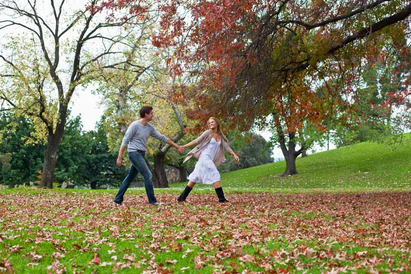 Young couple holding hands and walking through autumn leaves in a park