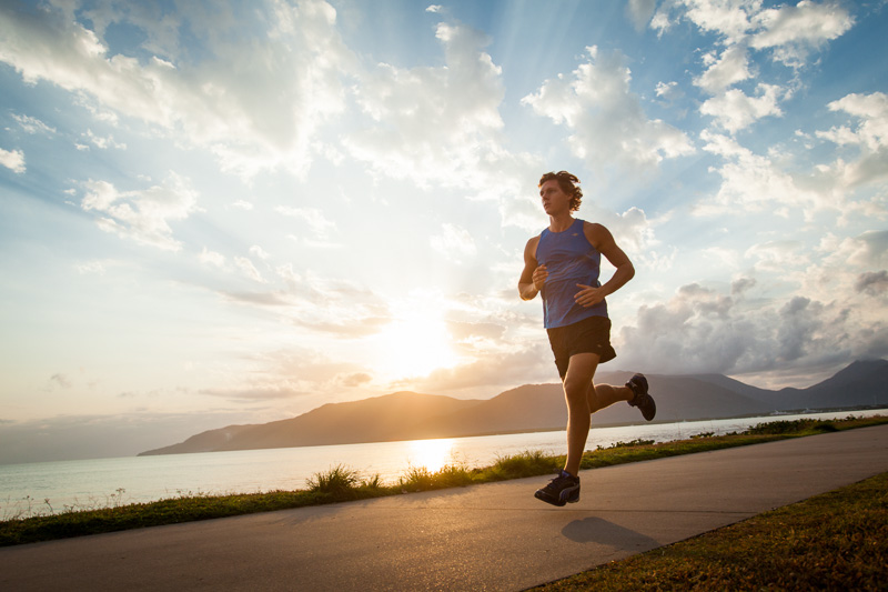 Young man running along the waterfront with sunrise beyond