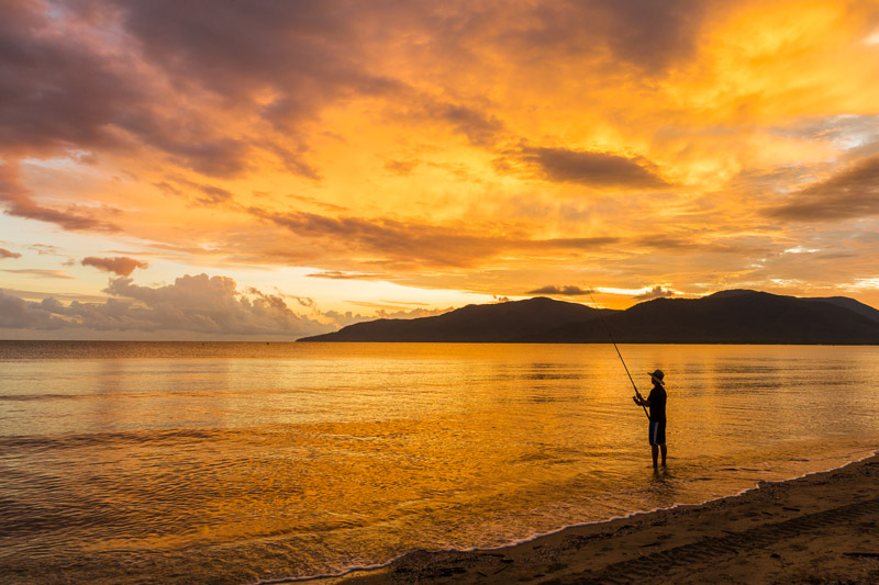 Fisherman standing in water is silhouetted against sunrise sky
