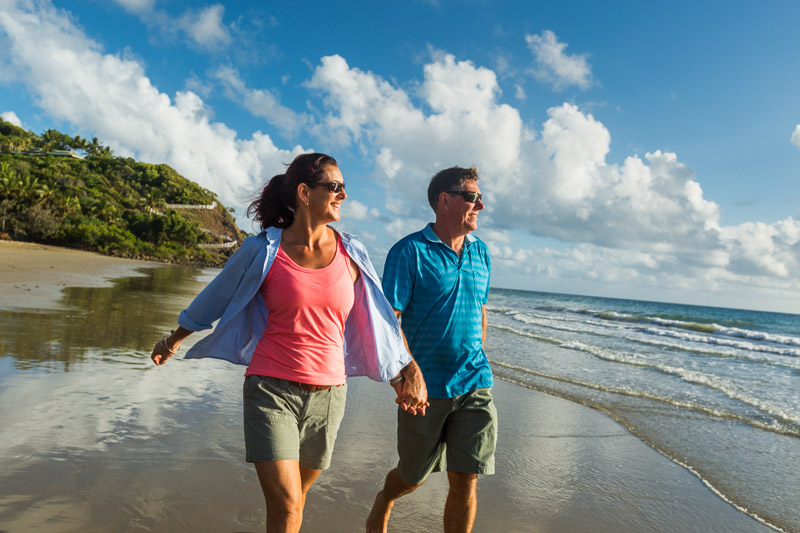 Mature couple walking along Four Mile Beach looking out to sea

