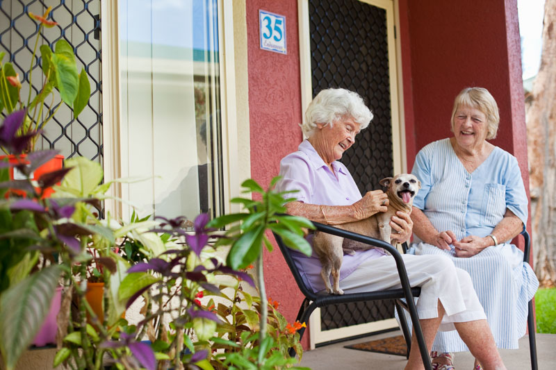 Aged resident with pet dog chatting to neighbour at assisted living community 