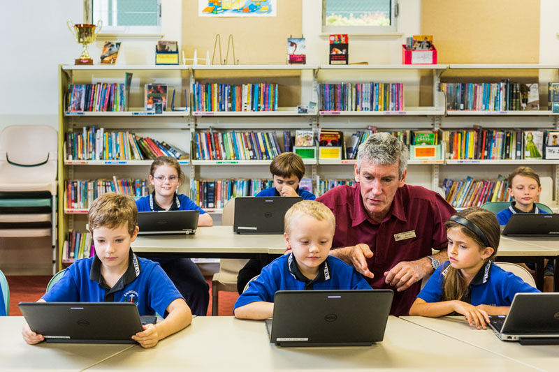 A teacher helping students looking at laptop computers in the classroom, Atherton Tablelands