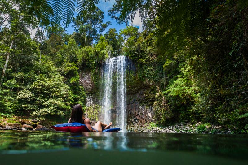 Woman relaxing on floating airbed looking at a tropical waterfall  
