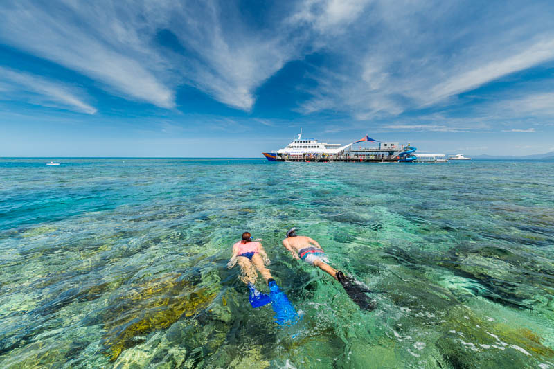 Couple snorkelling together on the Great Barrier Reef with reef pontoon in background
