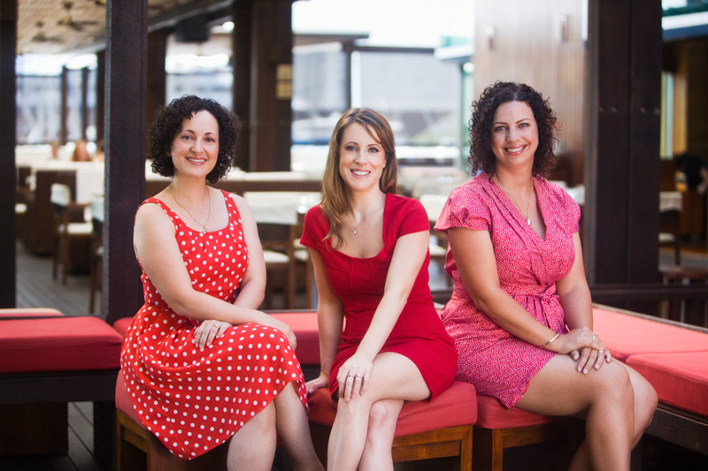 Group portrait of three businesswomen seated with restaurant backdrop, Cairns