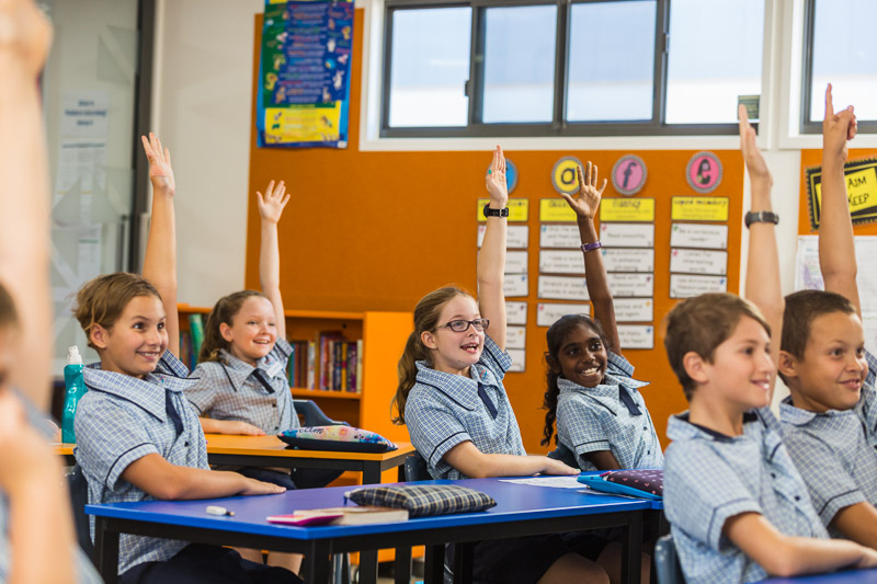 School students raise their hands to answer a question in the classroom