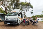 Group of young couples relaxing outside of campervan at riverside camping spot