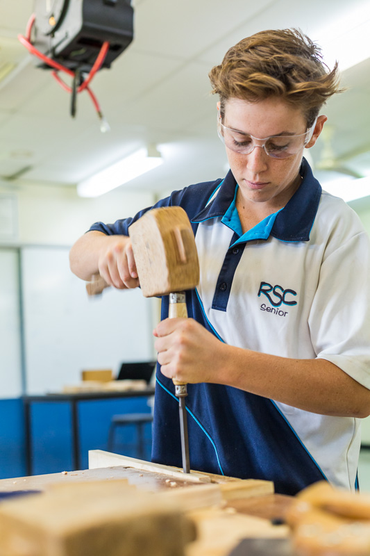 A high school student practising wood working skills with hammer and chisel