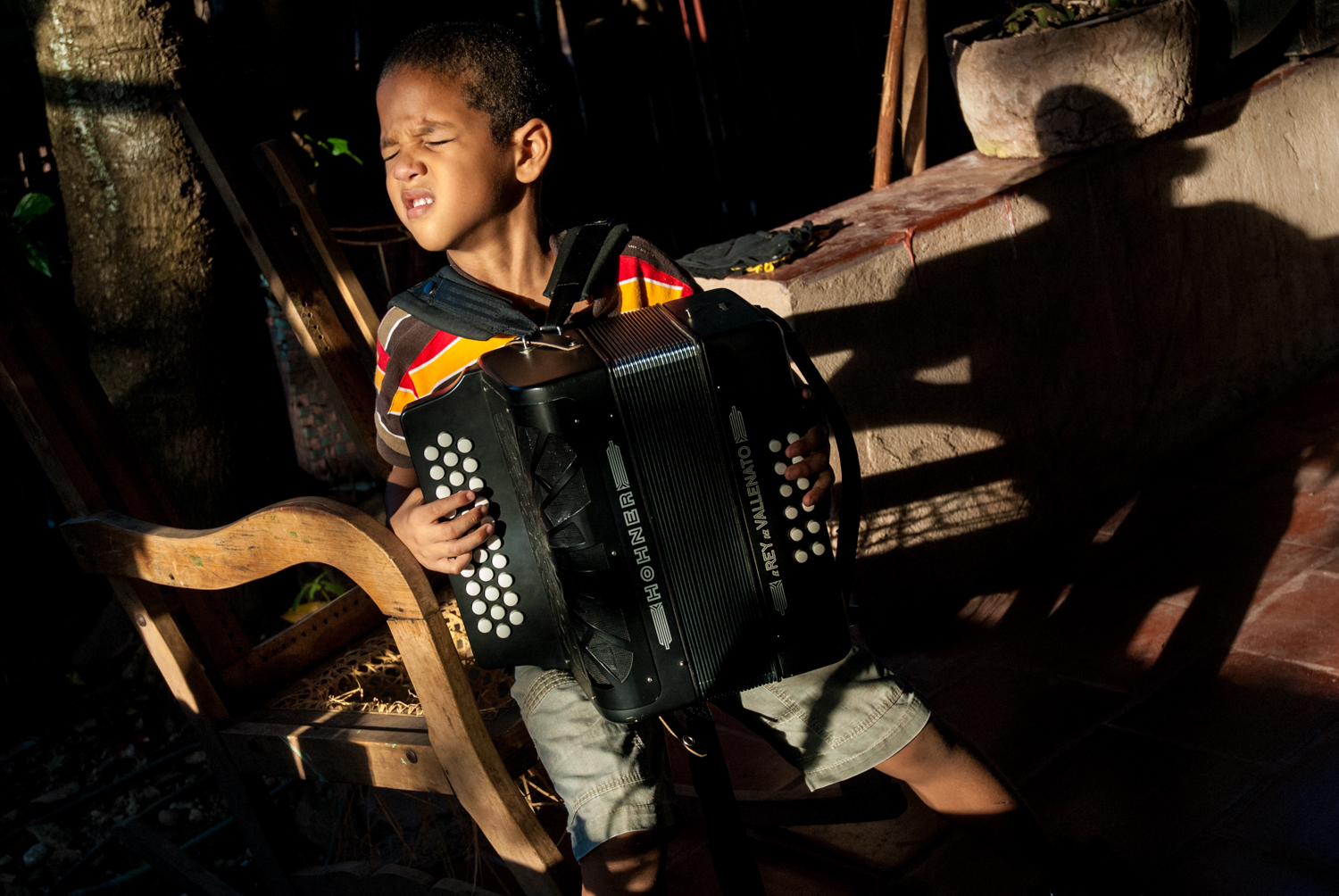 Mr. Dario Lopez's Vallenato music school in Villanueva. Youg boy practicing accordion.  Dario teaches mostly Acordion and holds his lessons in his home's patio. The accordion carries the melody in vallenato. Here the three row button model is used, known in different regions and at various times as “el moruno,” “guacamayo” and “espejito” (“machine screw”). The accordion first came to Colombia in the latter 1800s where it was used in European dance music. From the very beginning it was considered a lowbrow instrument, a position it proudly maintains to this day. Most accordions continue to be imported from Honer in Germany where they are tweaked to produce the warm and reedy sound Colombians prefer.