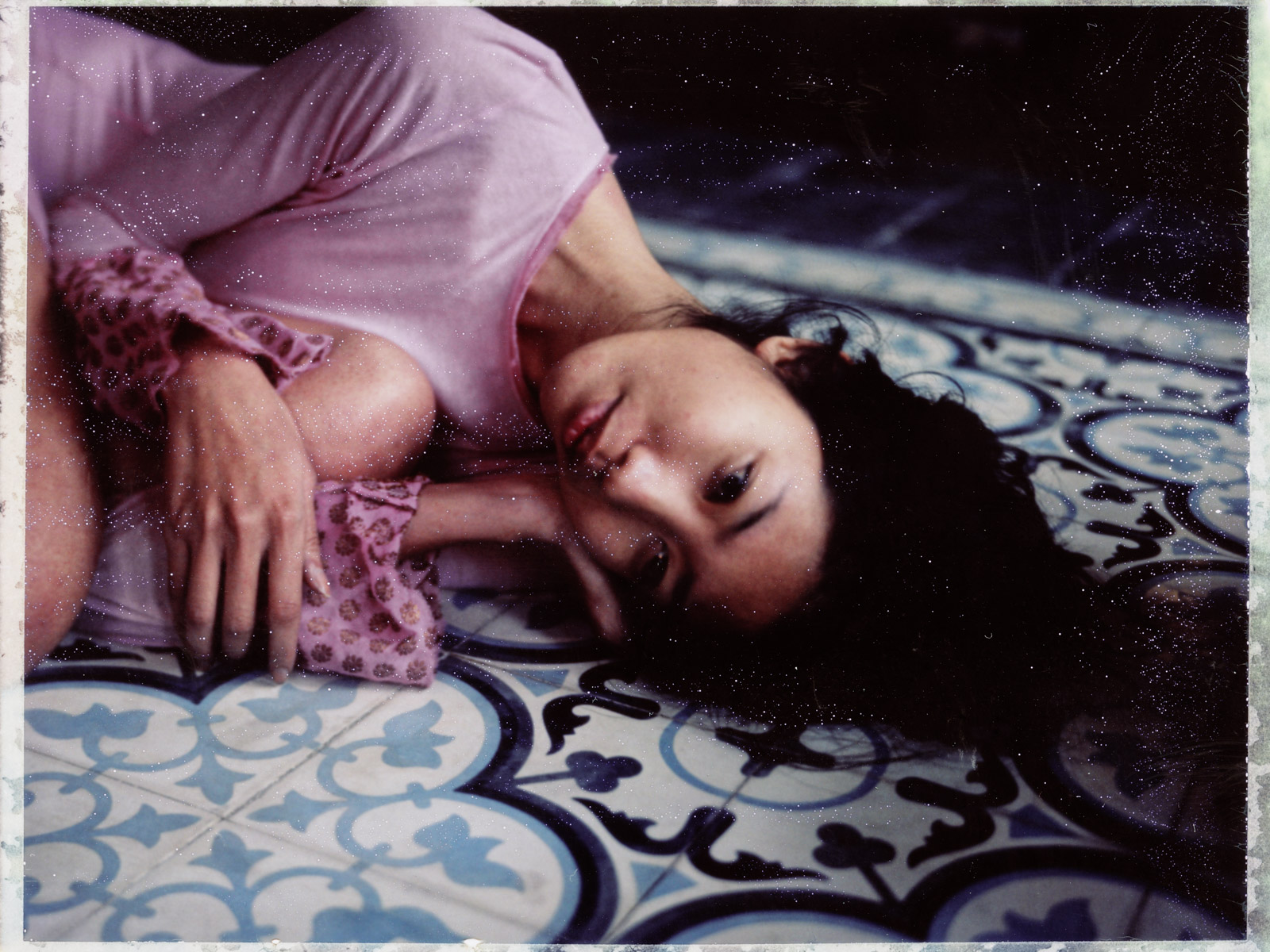 A Polaroid of a young woman in a pink top on a blue-tiled floor at an old home in Hanoi, Vietnam.