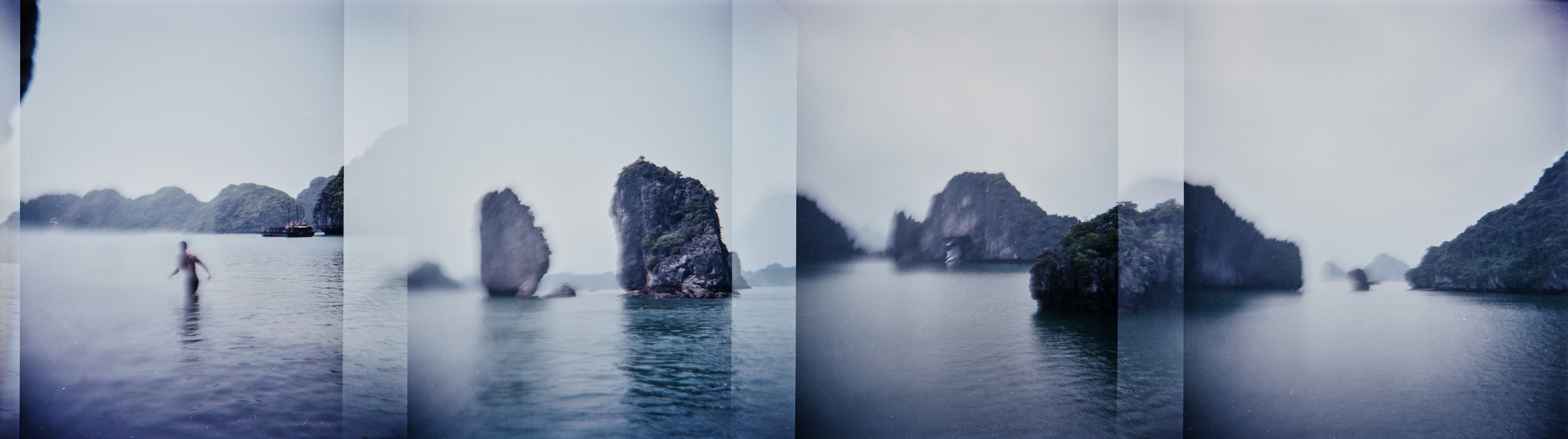 A panorama view of karsts and boats and a man walking in Halong Bay in northern Vietnam.