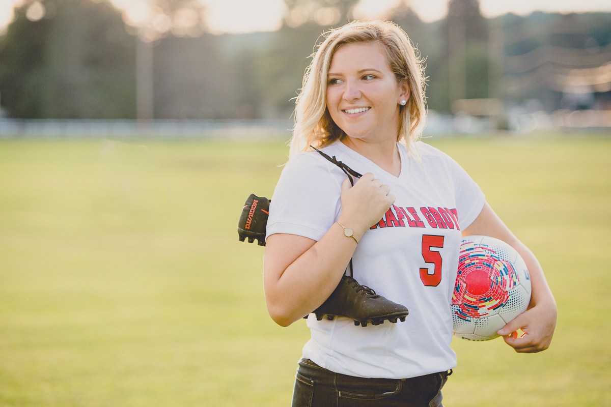 senior portrait by photographer Lindsay DeDario of maple grove high school student holding soccer ball and cleats in field in Bemus Point, a small town near Buffalo, NY in WNY 