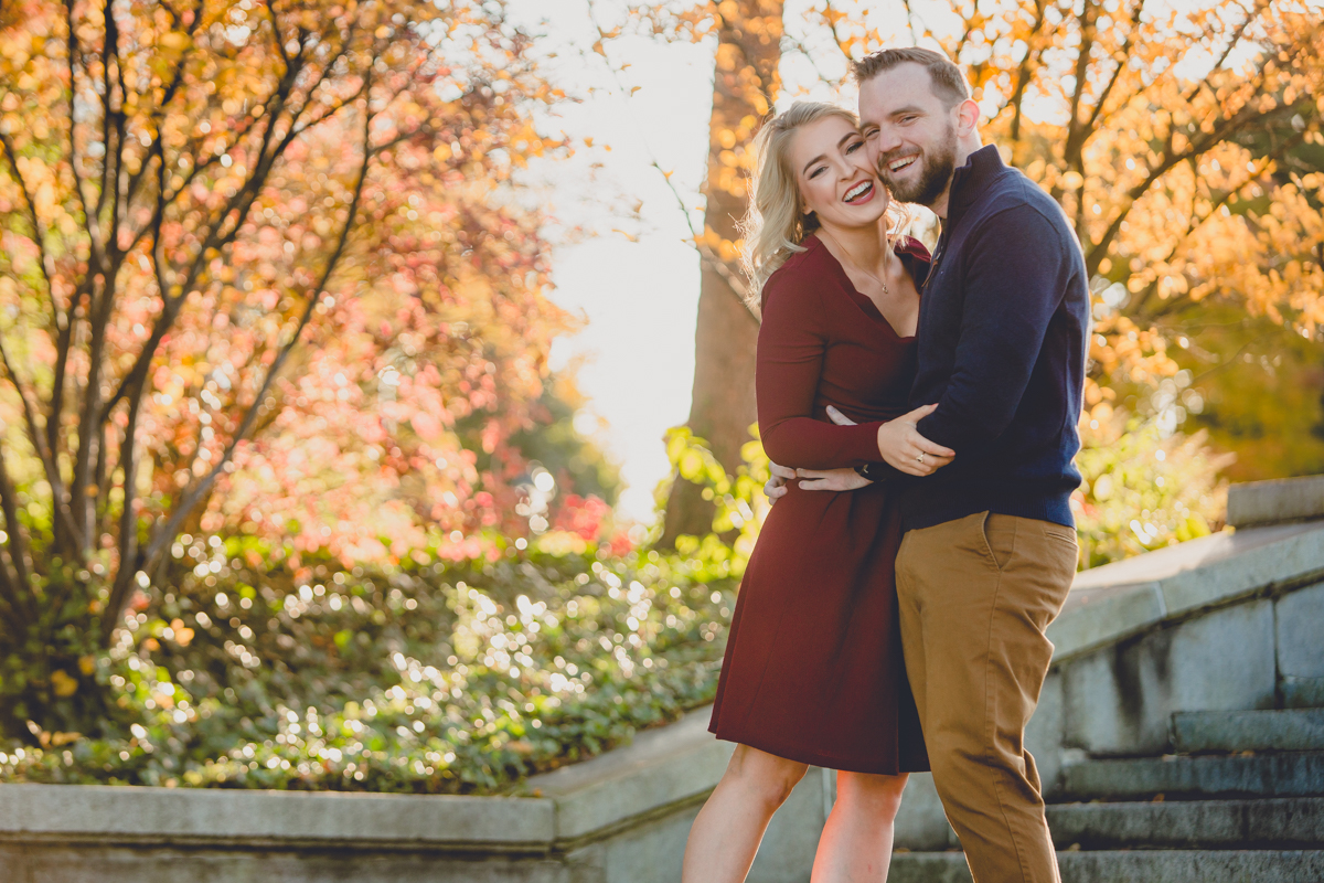 couple smiles for photographer during weddding engagment portrait photography session on steps to Hoyt Lake in Delaware Park in Buffalo, NY