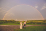 bride and groom hold hands under clear umbrellas beneath rainbow during their wedding reception at freedom run winery in WNY