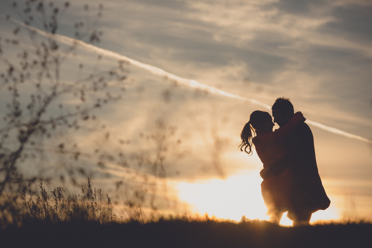 couple looks at each other in silhouette during sunset at buffalo harbor state park during wedding engagement photography session