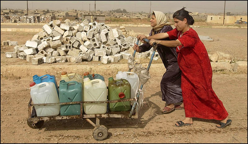 Kamal, front, pushes a cart of water back to her home with neighbor Mahaban Abdullah-Rahim. Kamal walks a mile three times a day to get water. 