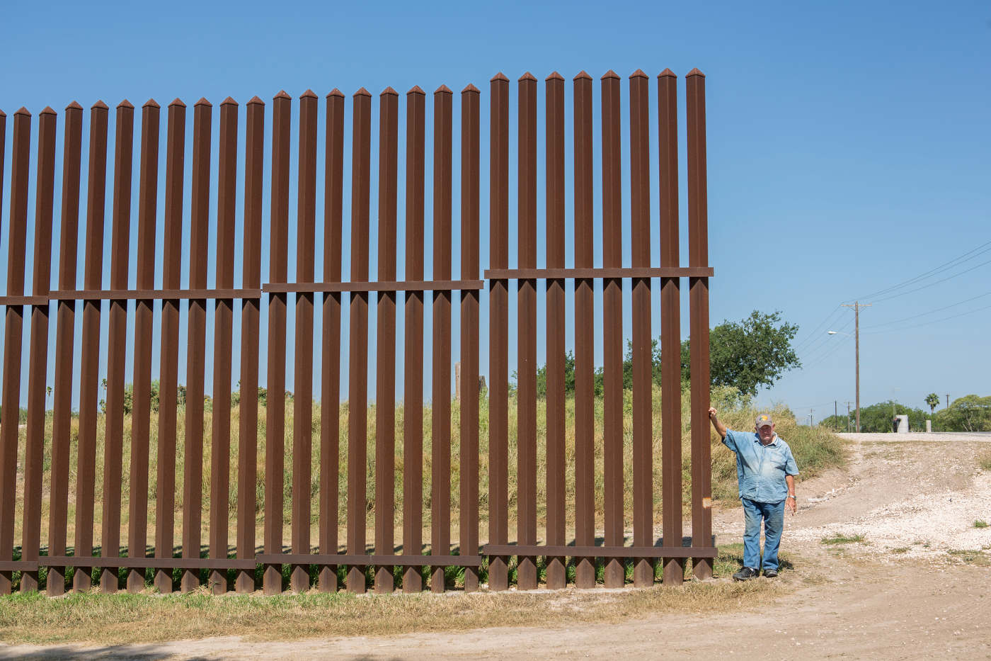 Rusty Monsees, an anti-immigration activist whose land is cut in half by the border wall, stands near the fence on his property.