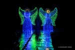 Colour photograph of Christmas Lights of two angels in blue and green and their reflection on the wet path