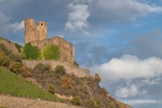 Colour photograph of the sun lighting up Ehrenfels Castle in profile on teh steep banks of the Middle Rhein in the state of Hesse in Germany with blue sky and clouds