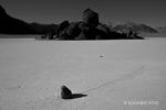 black and white photograph of a Rock and Race Trail at Racetrack. With high winds and wet lakebed the rocks are moved and have a trail behind them.