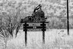 black and white photograph of teh Welcome to Patagonia sign of a silhouette stem train coming towards you