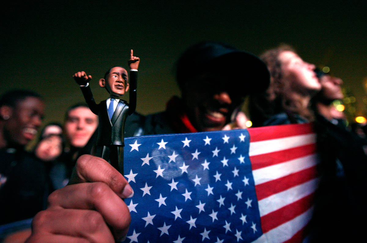Chinyere Brown of Chicago clutches her Obama doll and flag as she watches the results and waits in the unticketed area at Grant Park.