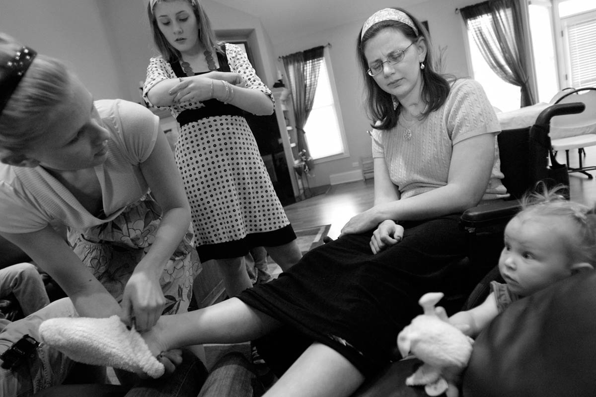 Courtney is surrounded by her neices Brooke Johnson, left, Brittney Henrie, 12, center left, and Kayla Dawn Johnson, 2, right, as they try to make her comfortable by putting warm socks on her feet. Courtney can speak, but is often confused by directions and has difficulty finding the right words to describe what she wants. 