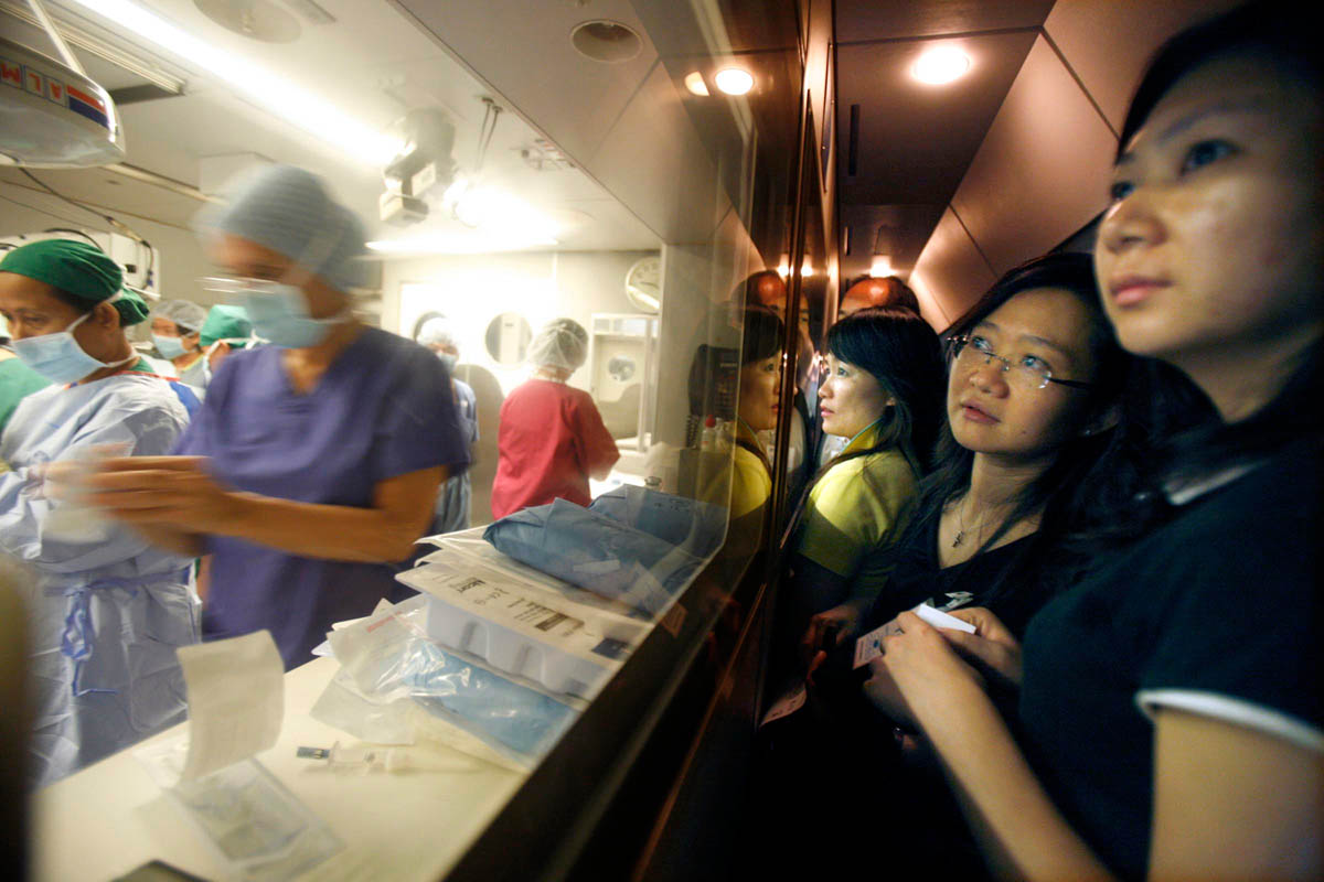A group of donors from Hong Kong peer through the viewing window into the operating theater aboard the ORBIS Flying Eye Hospital in Phnom Penh, Cambodia, December 13, 2007. 